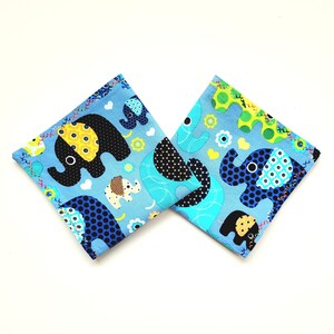 Könnte beinhalten: Zwei blaue Stoffquadrate mit weißem Hintergrund und bunten Elefantenmotiven. Die Elefanten sind schwarz, gelb und blau mit weißen Punkten.