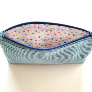 May include: A light blue zippered pouch with a colorful polka dot lining. The pouch is made of a soft, textured fabric.