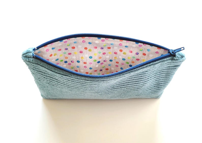 May include: A light blue zippered pouch with a colorful polka dot lining. The pouch is made of a soft, textured fabric.