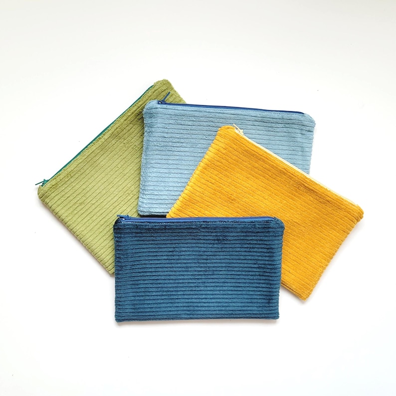 Könnte beinhalten: Vier Reißverschlusstaschen in verschiedenen Farben: Grün, Blau, Gelb und Dunkelblau. Die Taschen sind aus einem weichen, strukturierten Stoff.