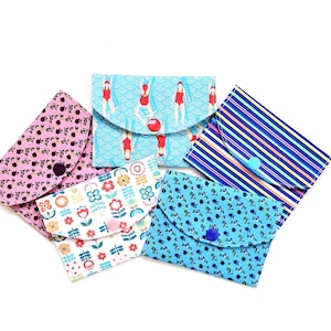 Könnte beinhalten: Fünf kleine Stoffbeutel mit Knopfverschlüssen. Die Beutel weisen verschiedene Muster auf, darunter Blumenmuster, Schwimmer in einem Pool und Streifen. Zu den Farben gehören Rosa, Blau und Weiß.