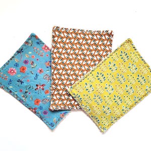 Könnte beinhalten: Drei Baumwoll-Geschirrtücher mit verschiedenen Blumenmustern. Eines ist blau mit rosa und orangefarbenen Blumen, eines ist braun mit weißen und orangefarbenen Mustern und eines ist gelb mit grünen und weißen Mustern.