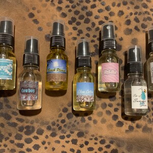 May include: Eight small glass bottles with spray tops and labels. The labels have various designs and text, including "Volcano", "Cowboy", "Beach Please", "Clean Cotton", "Pink Salt", "Sip of Summer", and "Cactus & Sea Salt".