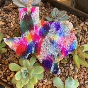 May include: A colorful tie-dye Texas state ornament with a white background. The ornament is made of leather and has a string for hanging.