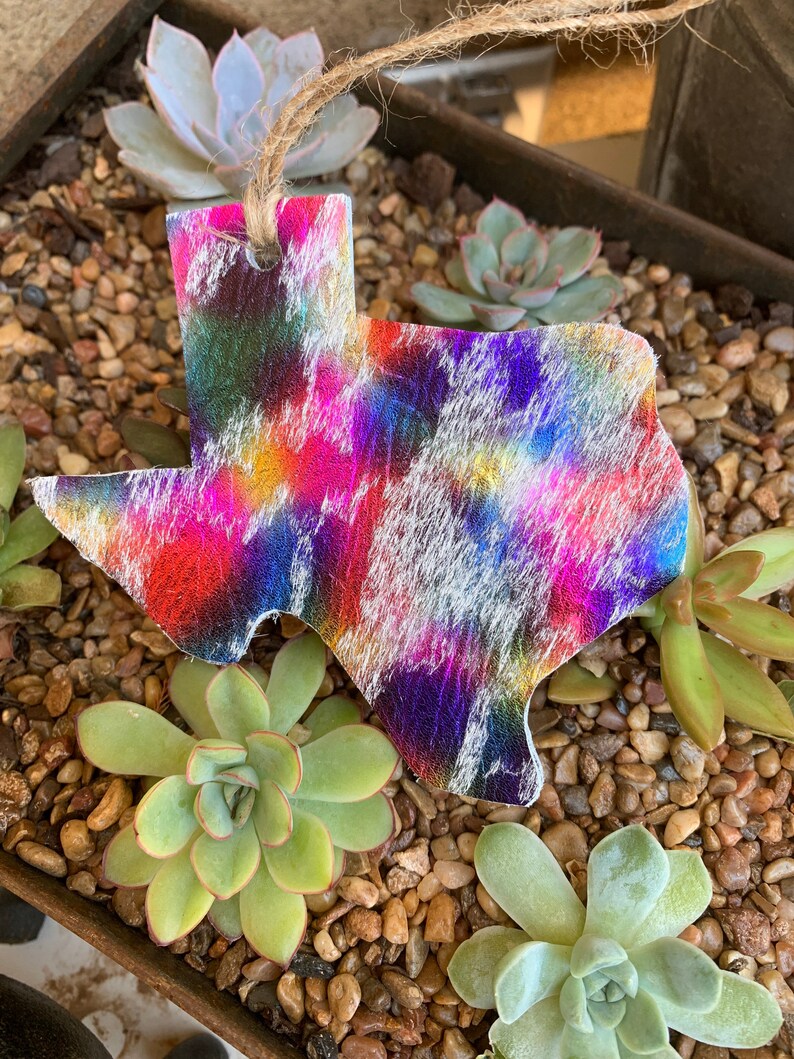 May include: A colorful tie-dye Texas state ornament with a white background. The ornament is made of leather and has a string for hanging.
