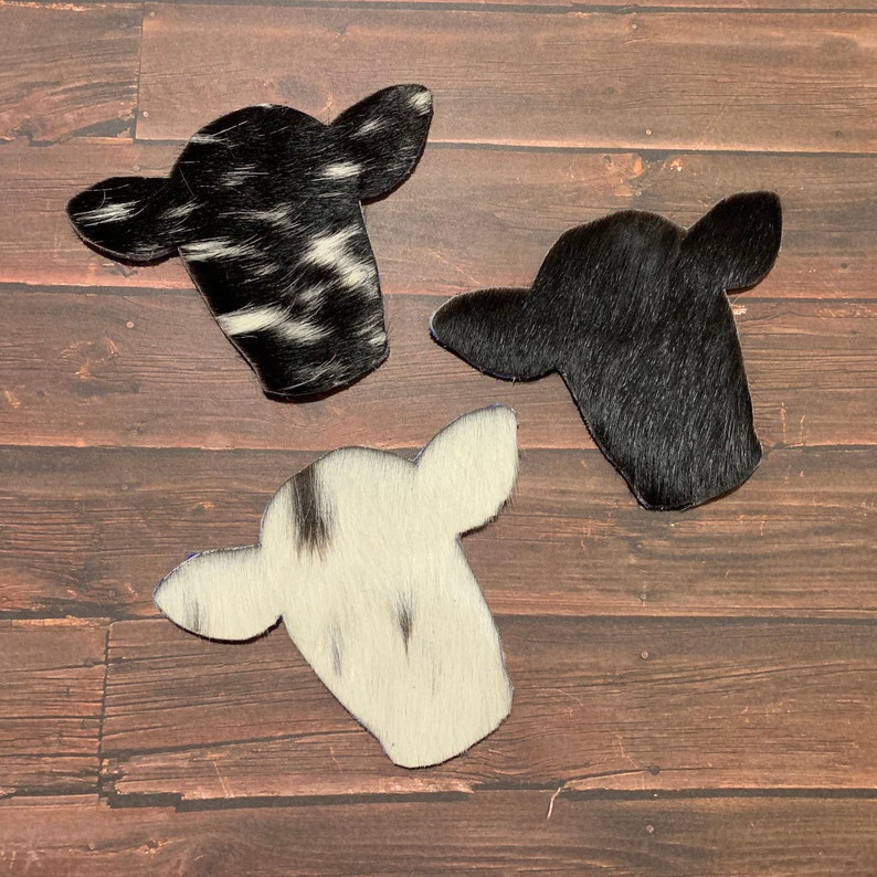 Puede incluir: Tres parches de piel de vaca en forma de cabeza de vaca. Los parches son blanco y negro, negro y blanco con manchas negras.