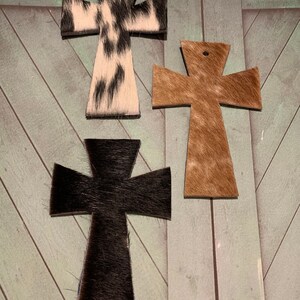 Puede incluir: Tres cruces de piel de vaca en diferentes colores y patrones. Las cruces son negras, marrones y blancas con manchas negras.