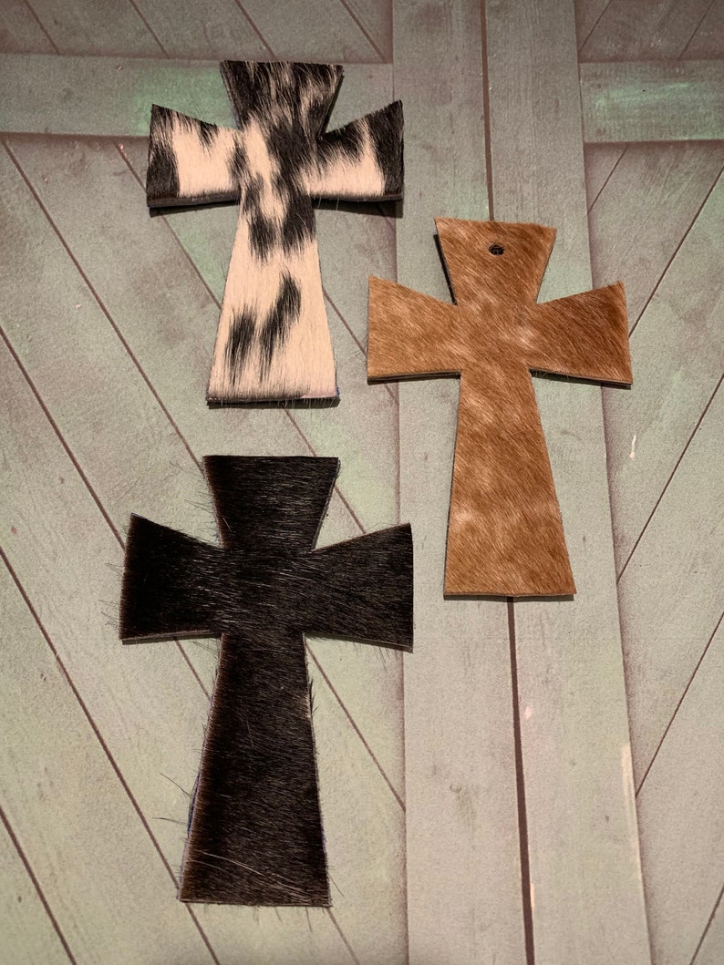 Puede incluir: Tres cruces de piel de vaca en diferentes colores y patrones. Las cruces son negras, marrones y blancas con manchas negras.
