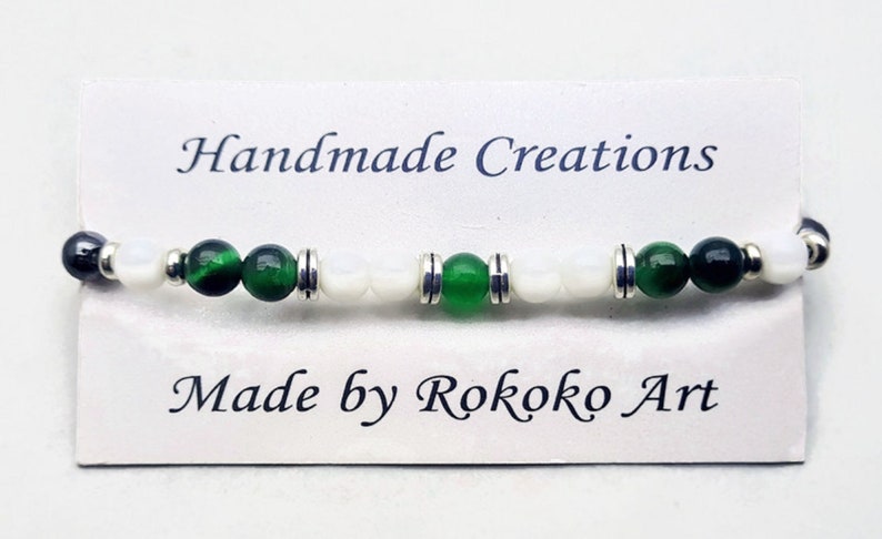 May include: A green and white beaded bracelet with silver accents. The bracelet is on a white card with the text "Handmade Creations" and "Made by Rokoko Art".