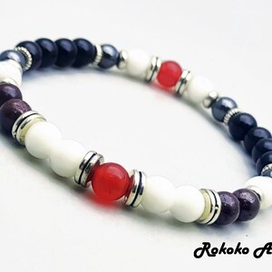 May include: A bracelet with black, white, red, and brown beads, separated by silver spacers. The bracelet has a silver clasp.