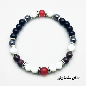 May include: A beaded bracelet with black, white, red, and brown beads. The bracelet has silver accents and is made with natural stones.