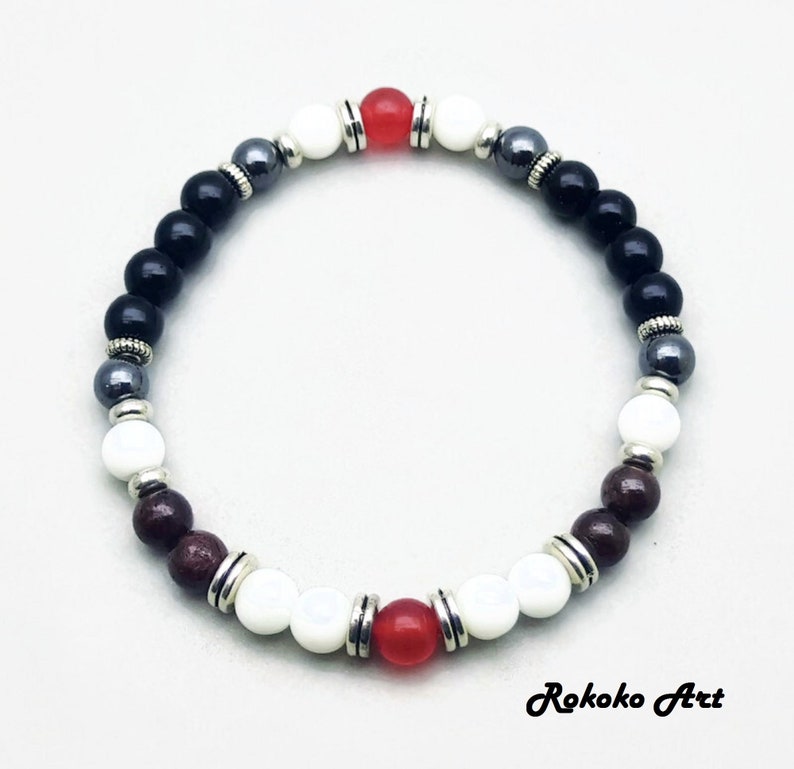 May include: A beaded bracelet with black, white, red, and brown beads. The bracelet has silver accents and is made with natural stones.