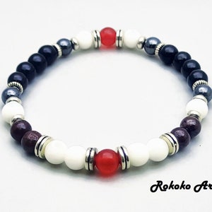 May include: A beaded bracelet with black, white, red, and gray beads. The bracelet has silver accents and is made with natural stones.