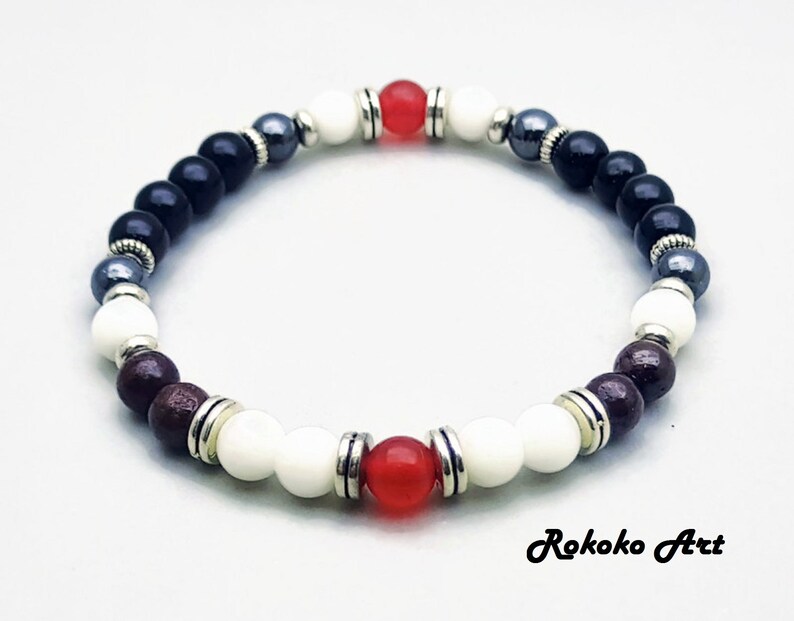 May include: A beaded bracelet with black, white, red, and gray beads. The bracelet has silver accents and is made with natural stones.