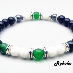 May include: A black, white, and green beaded bracelet with silver accents. The bracelet features green jade and tiger's eye beads.