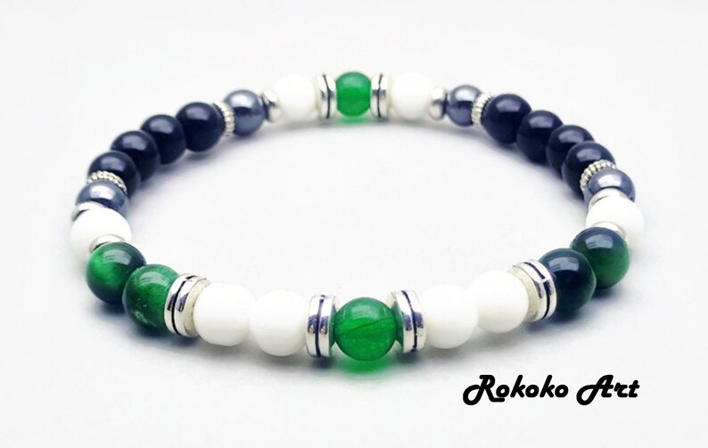May include: A black, white, and green beaded bracelet with silver accents. The bracelet features green jade and tiger's eye beads.