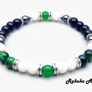 May include: A black, white, and green beaded bracelet with silver accents. The bracelet features green jade, black onyx, white howlite, and hematite beads.