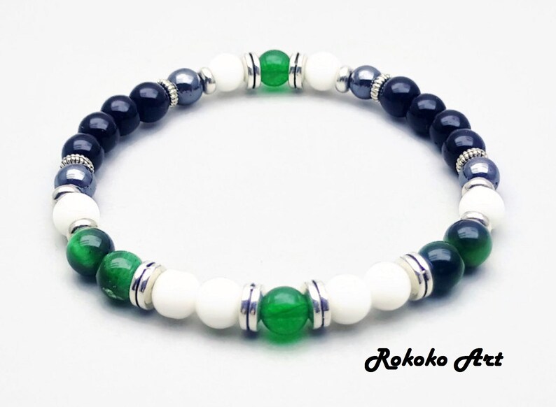 May include: A black, white, and green beaded bracelet with silver accents. The bracelet features green jade, black onyx, white howlite, and hematite beads.