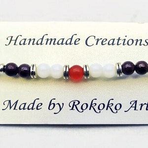 May include: Handmade bracelet with white, brown, and red beads. The bracelet is on a white card with the text "Handmade Creations" and "Made by Rokoko Art".