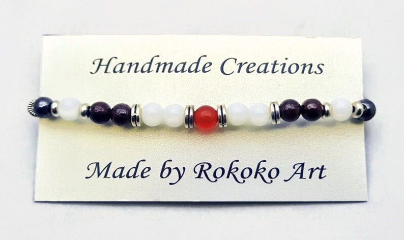 May include: Handmade bracelet with white, brown, and red beads. The bracelet is on a white card with the text "Handmade Creations" and "Made by Rokoko Art".
