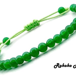 Puede incluir: Una pulsera de cuentas verdes con cierre de nudo corredizo. La pulsera presenta cuentas redondas pulidas y un cordón verde claro. El texto "Rokoko Art" está en la esquina inferior derecha.