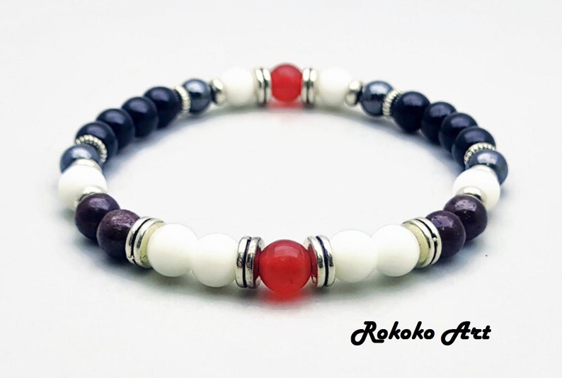 May include: A beaded bracelet with black, white, red, and brown beads. The bracelet has silver accents and is made with natural stones.