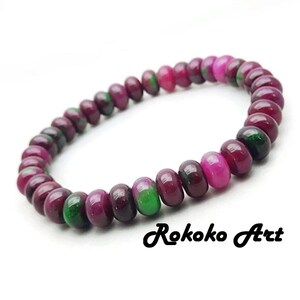 May include: A beaded bracelet featuring a series of round, polished gemstones in shades of deep red, pink, and green. The bracelet is strung together, creating a flexible band. The text "Rokoko Art" is in the lower right corner.