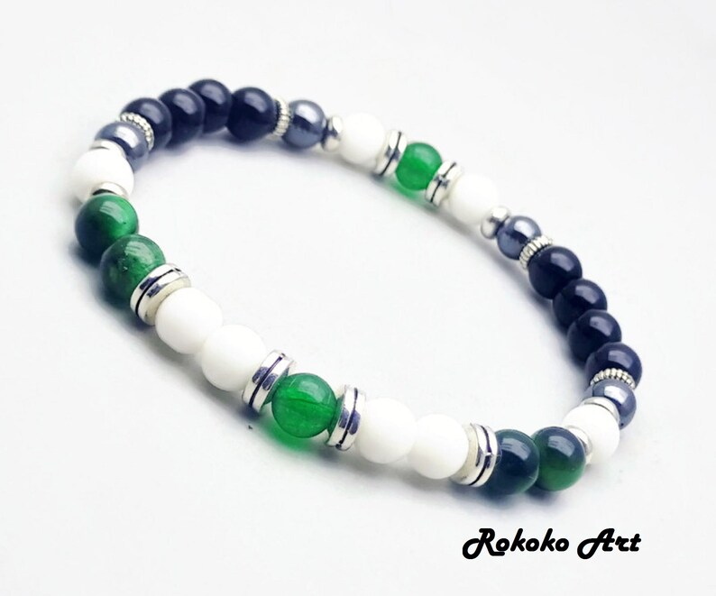 May include: A bracelet with black, white, and green beads, separated by silver spacers. The bracelet is made of natural stones and is a stylish accessory.
