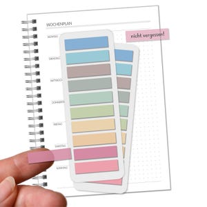 Könnte beinhalten: Ein Wochenplaner mit Spiralbindung und farbigen Haftnotizen. Die Notizen sind in Pastelltönen wie Blau, Grün und Rosa gehalten. Der Text "nicht vergessen!" ist auf einem rosa Haftzettel zu sehen.
