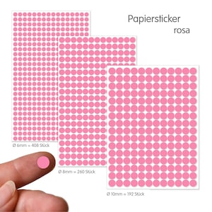 Op de afbeelding: Drie vellen roze stipstickers in diameters van 6 mm, 8 mm en 10 mm. De tekst "Papiersticker rosa" staat boven de stickers. Een vinger houdt een enkele roze sticker vast.