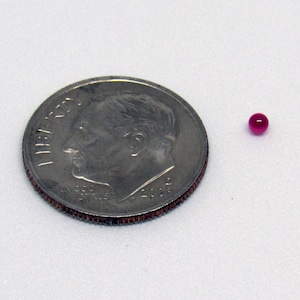 May include: A small, bright pink, round bead next to a US dime coin.