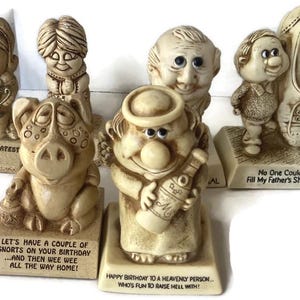 May include: Set of six whimsical ceramic figurines with humorous sayings. Each figurine is hand-painted and features a unique character with a quirky expression. The sayings include "World's Greatest Mom", "Let's Have a Couple of Snorts on Your Birthday...and Then Wee Wee All the Way Home!", "Happy Birthday to a Heavenly Person...Who's Fun to Raise Hell With!", "No One Could Fill My Father's Shoes", and two other sayings.