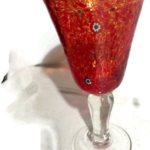 May include: A red glass goblet with a textured surface and white and black flecks throughout. The goblet has a clear glass stem and base.