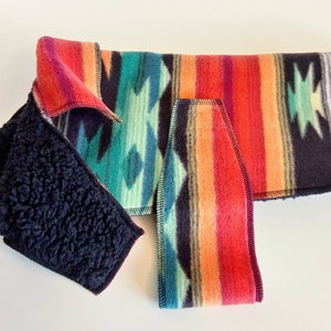 May include: A black fleece dog coat with a colorful southwestern pattern. The coat has a zipper closure and a fleece lining. The coat is laid flat on a white surface.