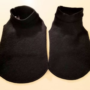 May include: Two black turtleneck dog sweaters, one larger than the other, laid out on a white surface.