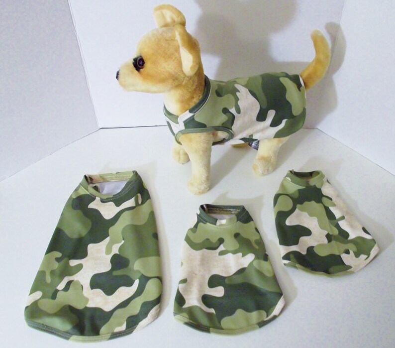 May include: Four camouflage dog shirts in different sizes. The shirts are green and tan with a camouflage pattern.