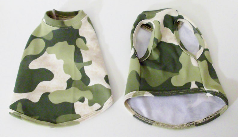 May include: Two camouflage dog shirts, one with short sleeves and one sleeveless. Both shirts are green and beige with a camouflage pattern.