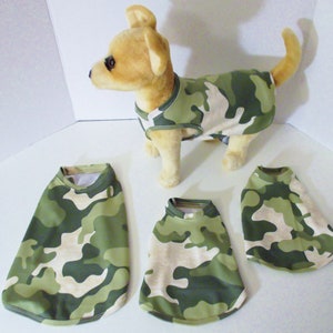 May include: Four camouflage dog shirts in green and tan. The shirts are sleeveless and have a round neckline. One shirt is being worn by a small, light brown dog.