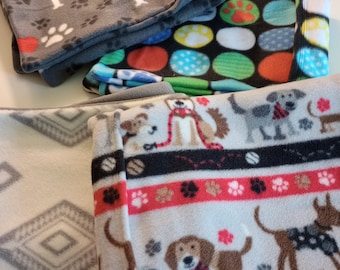 May include: Four fleece dog blankets with different patterns. One blanket is gray with paw prints and the words "I love" on it. Another blanket is black with colorful polka dots. The third blanket is white with a red, black, and white striped pattern and a repeating pattern of dogs. The fourth blanket is white with a gray diamond pattern.
