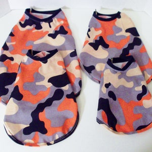 May include: Four dog shirts in different sizes, all featuring a camouflage pattern in shades of orange, black, gray, and beige.
