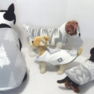 May include: Four dogs wearing different grey and white patterned fleece dog sweaters. The sweaters have a geometric design.
