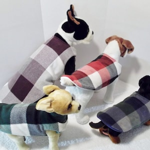 May include: Four dogs wearing plaid fleece dog coats in different colors: burgundy, red, green, and blue. The coats have a white background with plaid patterns in different colors.