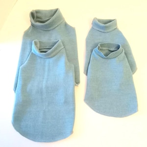 May include: Four light blue turtleneck sweaters. Two are larger, with long sleeves, and two are smaller, with shorter sleeves. The sweaters are made of a soft, knit material and are designed for pets.