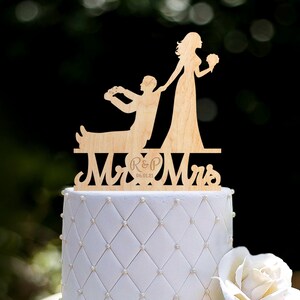 Puede incluir: Topper de pastel de boda de madera con una novia tirando de un novio en una silla. El topper dice "Mr & Mrs" con las iniciales "R & P" y la fecha "06.01.21".