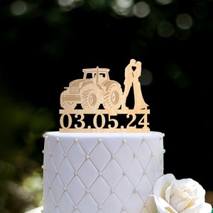 Könnte beinhalten: Holz-Tortenaufsatz für Hochzeit mit einer Silhouette eines sich küssenden Paares vor einem Traktor. Der Aufsatz enthält auch das Datum "03.05.24".