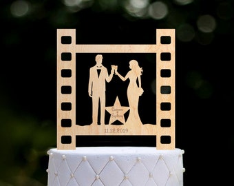 May include: Wooden wedding cake topper featuring a film strip frame with a silhouette of a couple toasting, a star with the names "Cameron & Sydney" and the date "11.12.2019".