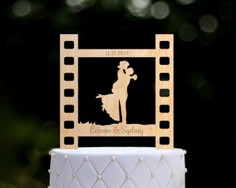 May include: Wooden wedding cake topper featuring a silhouette of a couple embracing, with the date "11.12.2019" and the names "Carson & Sydney" inscribed below. The topper is shaped like a film strip.