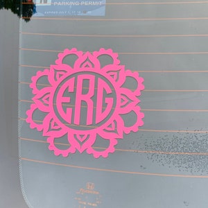 Peut inclure: Autocollant de voiture rose avec un monogramme des lettres "ERG" dans un cercle entouré d'un motif floral décoratif.