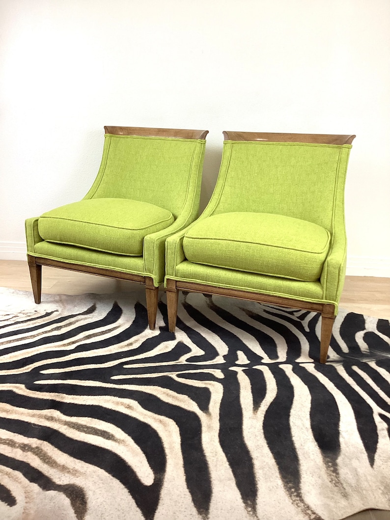 May include: Two lime green upholstered armchairs with wooden frames and legs. The chairs have a curved back and a square seat cushion. The chairs are placed on a zebra-striped rug.