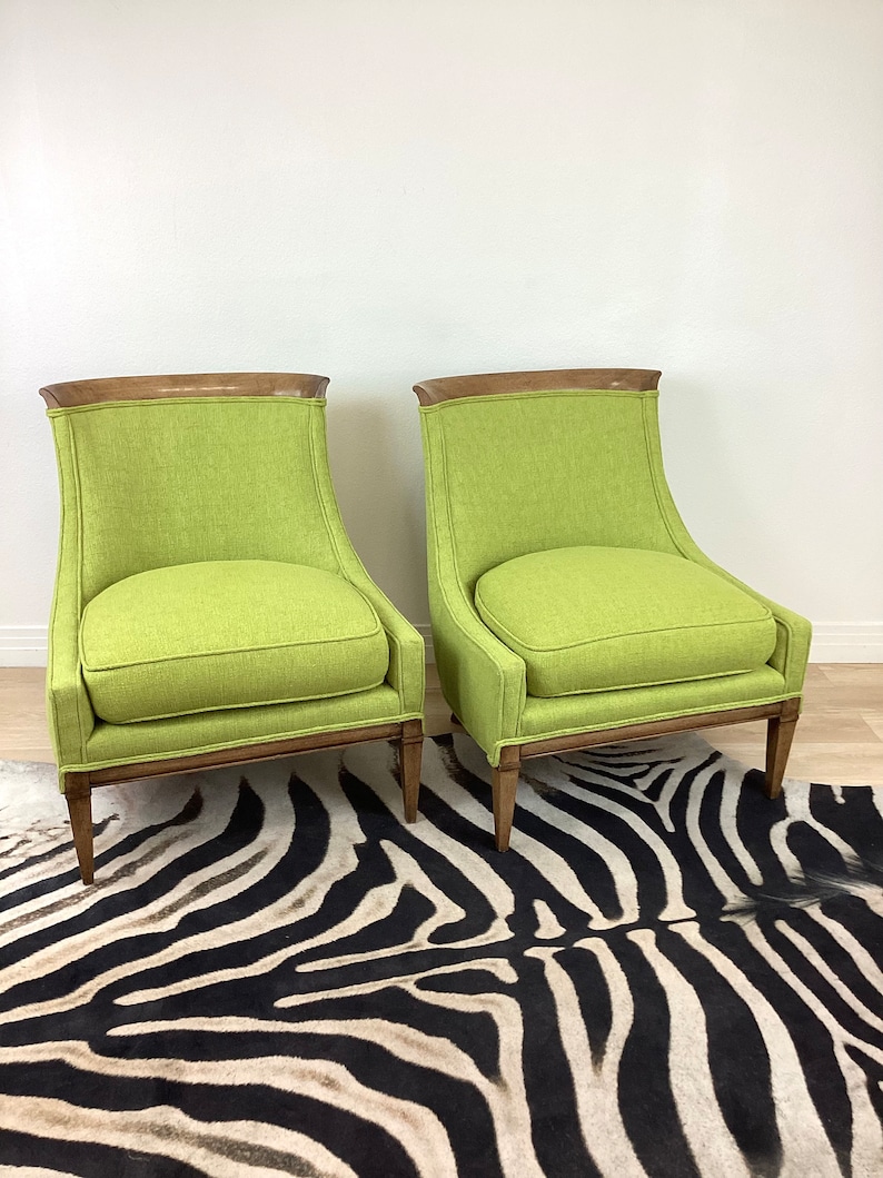 May include: Two lime green upholstered armchairs with wooden frames and legs. The chairs have a curved back and a cushioned seat. The chairs are placed on a zebra print rug.